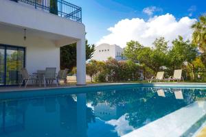 a swimming pool with chairs and a table next to a house at Azzurro Holiday Villas in Peyia