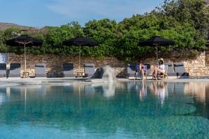 two people sitting under umbrellas next to a swimming pool at Paros Agnanti Resort & Spa in Parikia