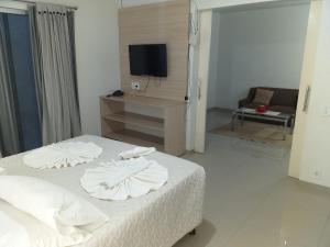 a bedroom with a bed with white sheets and a tv at Lisboa Palace Hotel in Alta Floresta