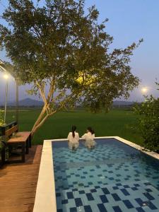 two women sitting next to a swimming pool at Nana Field Cabin 3 in Ban Phra Fang