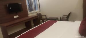 een slaapkamer met een bed en een bureau met een televisie bij Butola Hotels in Rishīkesh