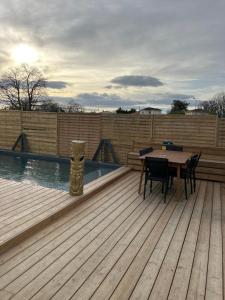 a wooden deck with a table and a swimming pool at Aux portes de bordeaux Maison cocooning avec Piscine spa chauffé in Ambarès-et-Lagrave