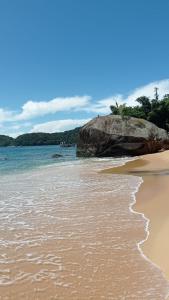 a sandy beach with a large rock and the ocean at Pousada Sobre A Rocha in Praia de Araçatiba