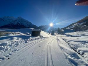 una carretera cubierta de nieve con el sol en el fondo en Alpenpension Elferblick, en Hirschegg