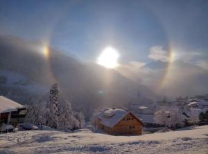 un pueblo cubierto de nieve con el sol en el cielo en Alpenpension Elferblick, en Hirschegg