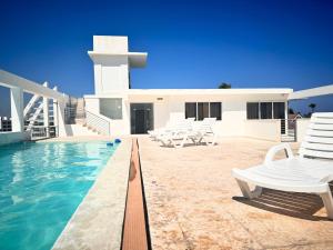 een zwembad met witte stoelen en een huis bij ATLANTICO SUITES - ROOFTOP POOL, BARS & BEACH CLUB in Punta Cana