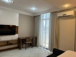 um quarto com uma televisão, uma secretária e uma janela em Millenium Hotel Flat em Manaus