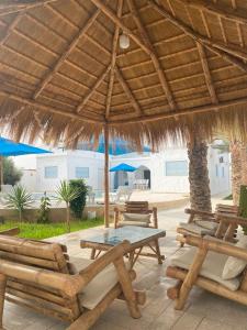patio ze stołem i krzesłami pod słomianym parasolem w obiekcie Villa La Palmeraie d'Arkou, grande piscine w mieście Arkou