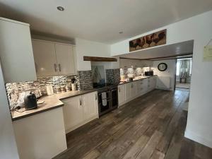 a large kitchen with white cabinets and wooden floors at Five Farthings Stylish cottage in Littleworth