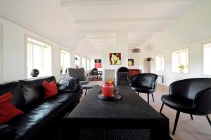a living room with a black leather couch and chairs at Hygge Ho - mitten in der Natur mit Sauna und Spa in Blåvand