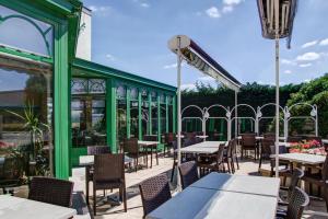 a patio with tables and chairs and a green building at LOGIS Hotel l'Escargotière Dijon Sud - Chenove in Chenôve
