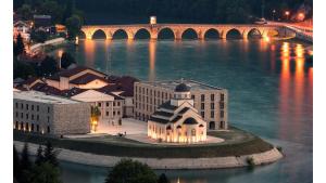 a building on the river with a bridge in the background at Apartman D in Višegrad