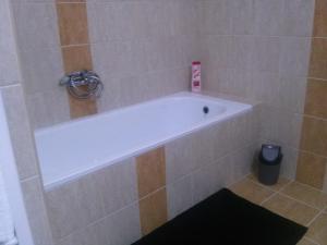 La salle de bains carrelée est pourvue d'une baignoire blanche. dans l'établissement Fészek Apartman, à Debrecen