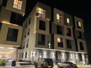 dos autos estacionados frente a un edificio por la noche en Luxurious Three Bedroom Apartment North of Riyadh شقة فخمة مكونة من ثلاث غرف نوم شمال الرياض en Riad