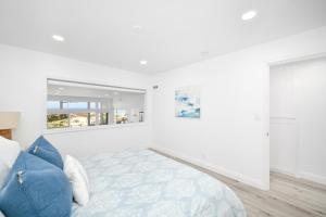 een witte slaapkamer met een blauw bed en een raam bij Brand new Lower unit on the Beach with Patio and Firepit in Newport Beach