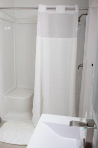 La salle de bains est pourvue d'un rideau de douche blanc et d'un lavabo. dans l'établissement The Sage Motel, à Saratoga