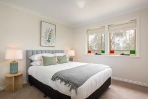 カトゥーンバにあるStunning Katoomba Home with Lush Garden&Playgroundの大きなベッドと2つの窓がある寝室