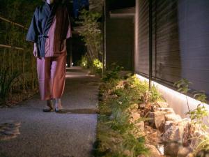 une femme marchant sur un trottoir la nuit dans l'établissement 湯本庵清姫, à Kirishima