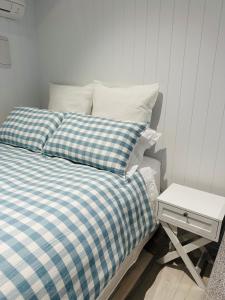 a bed with blue and white plaid sheets and a side table at Hobbiton Pool House in Matamata
