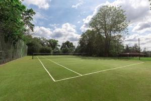 un court de tennis avec un filet dans un champ dans l'établissement Large Villa Mansion With Pool House & Tennis Court, à Potters Bar
