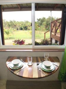 einem Holztisch mit Tellern und Gläsern und einem Fenster in der Unterkunft The Tiki Toucan Tropical Suite + Private Pool in Placencia Village