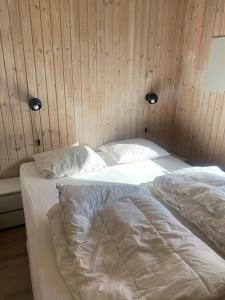 een slaapkamer met 2 bedden met witte lakens en houten wanden bij Skønt sommerhus tæt på skov, strand og hyggeligt havnemiljø in Bønnerup