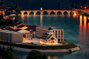 a building on the river with a bridge in the background at Hotel Andrićgrad in Višegrad