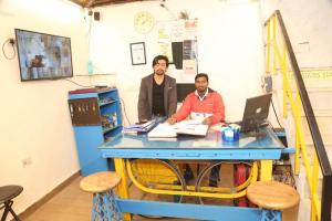 deux hommes assis à une table bleue avec un ordinateur portable dans l'établissement Bunk Hostel Delhi Best Backpacking Accommodation, à New Delhi