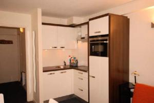 una pequeña cocina con armarios blancos y nevera. en Résidence MARMOTTES - Studio pour 4 Personnes 004 en Gourette