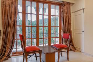 una mesa y 2 sillas frente a una gran ventana en Collection O Sukhsagar Resort, en Lonavala