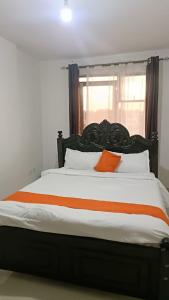 Runda Royale 3 bedroom apartment, Kiambu Road في Kiambu: سرير كبير مع وسائد برتقالية وبيضاء ونوافذ