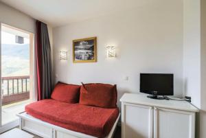 Habitación con sofá rojo, TV y ventana. en Résidence Le Thabor - maeva Home - Appartement 2 Pièces 5 Personnes - Confo 45, en Le Désert