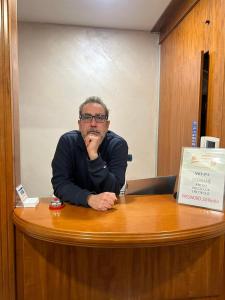 mężczyzna siedzący przy biurku z ręką na ustach w obiekcie Hotel Ercoli House w Rzymie