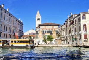 a yellow boat on a canal in front of buildings at ca dei zoti3 with luggage room in Venice