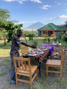 Lake Natron Maasai Guesthouse في Mtowabaga: رجل يقف أمام طاولة