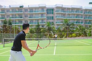 un homme tenant une raquette de tennis sur un court de tennis dans l'établissement OCEAN VISTA, à Phan Thiết