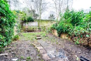 un jardín abandonado con una pared de piedra y árboles en Heart of Hackney - 2bed garden flat sleeps 6 en Londres