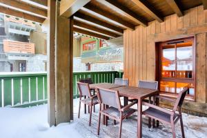 une table et des chaises en bois sur une terrasse couverte dans la neige dans l'établissement Résidence Les Arcs Le Village - maeva Home - Appartement pièces - Prestige 494, à Bourg-Saint-Maurice