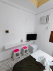 a white bedroom with a bed and two stools at Mini suíte Atitude Maragogi Centro in Maragogi