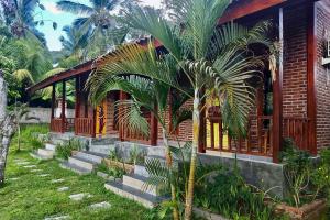 a house with a palm tree in front of it at Kampung Coklat Jembrana Mitra RedDoorz in Jembrana