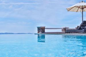 a swimming pool with an umbrella and some chairs and an umbrella at Exquisite Mykonos Villa - Villa Lakima - 6 Bedroom - Infinity Pool - Panoramic Sea And Sunset View - Pool Bar in Fanari