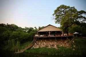a building with a tent on the side of a river at Zambezi Dusk in Livingstone