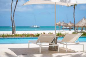 - deux chaises blanches et un parasol à côté de la piscine dans l'établissement Hyatt Regency Aruba Resort & Casino, à Palm-Eagle Beach