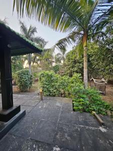 a patio with a palm tree and a bench at Patil's Greenwoods FarmHouse in Navi Mumbai