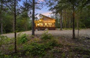 a log cabin in the woods with lights on at BRAND NEW!! Hochatown, Honey! Fire pit, hot tub, luxurious shower! in Broken Bow