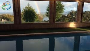 un arco iris visto a través de las ventanas de una casa con piscina en CABAÑA AZUL Y VERDE, en Ancud