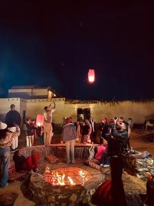 a group of people standing around a fire at night at Aghurmi Siwa Ecolodge & Salt Cave in Siwa +80 photos