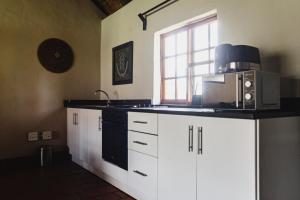 cocina con armarios blancos, microondas y ventana en Ardmore Guest Farm, en Champagne Valley