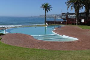 a swimming pool next to the ocean with palm trees at Beach Club Unit 207 in Mossel Bay