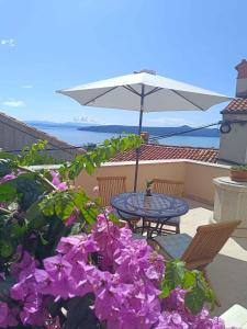 a table and chairs with purple flowers and an umbrella at Holiday home in Moscenice 15209 in Mošćenice